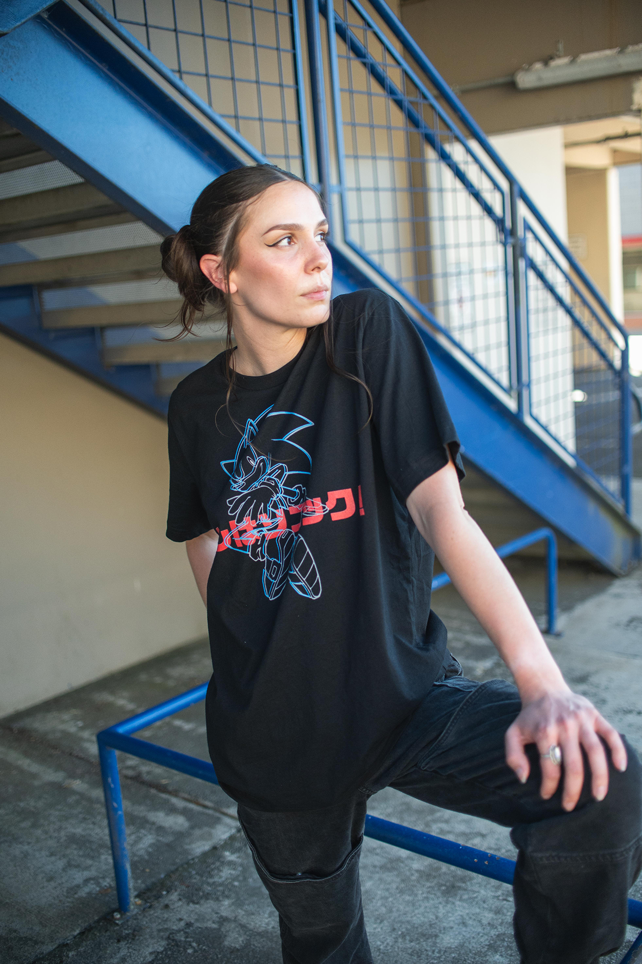 Person wearing a black t-shirt with a graphic design, sitting on a blue metal staircase.
