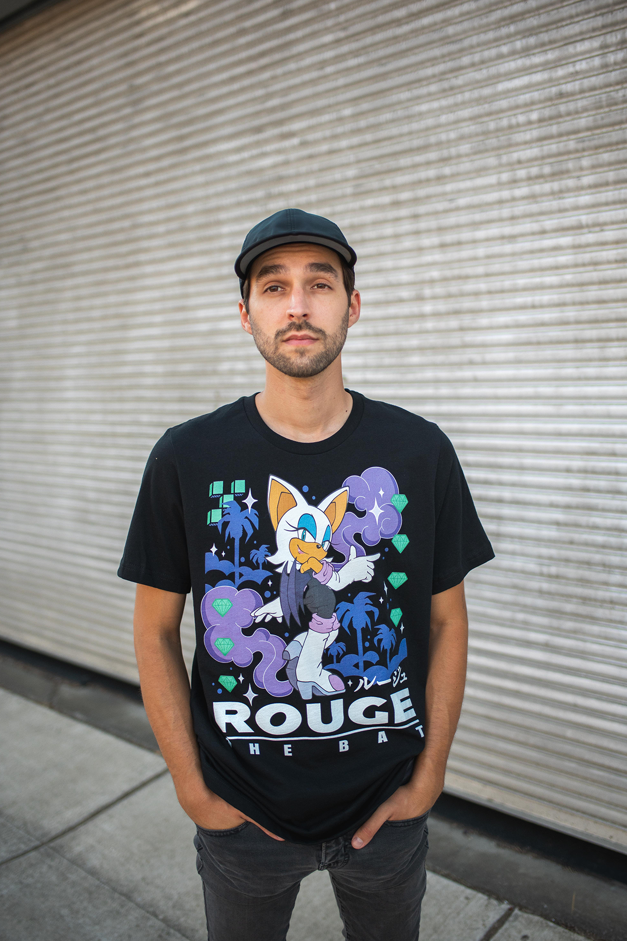 Man wearing a black t-shirt with a graphic design in front of a metallic shutter.